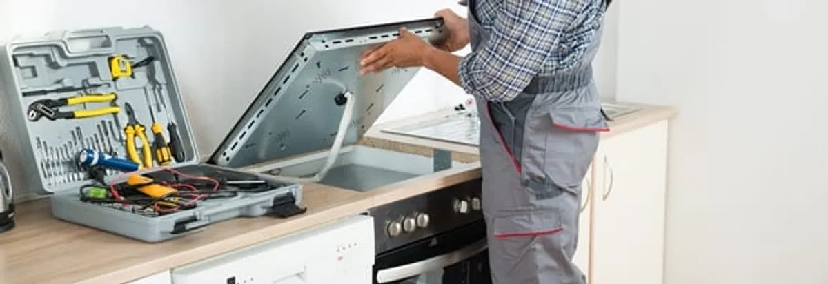 Cooktop repair technician lifting a built-in stovetop for service in Boston, MA